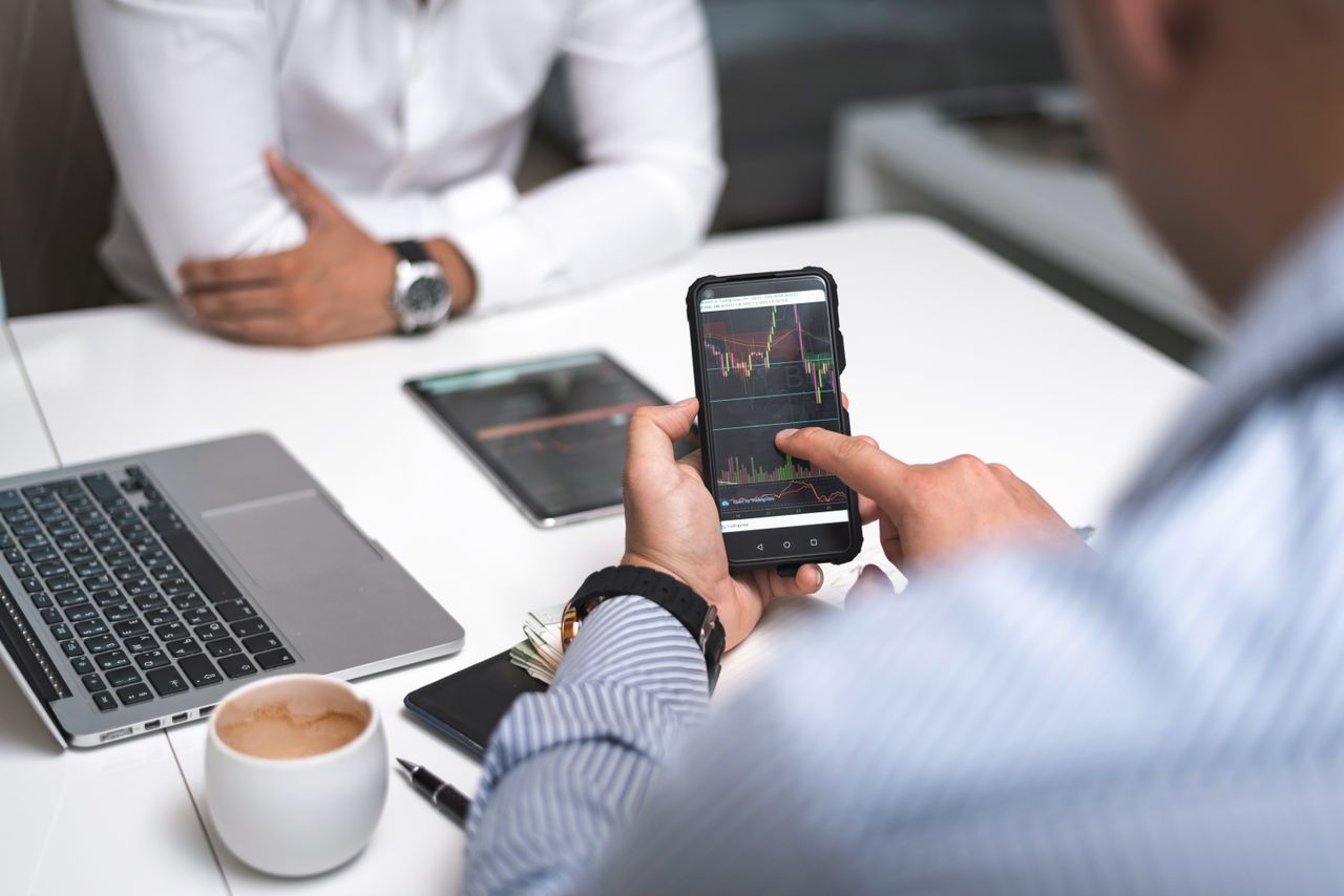 The Art of Drawing Readers In: Your attractive post title goes here Two businessmen analyze stock market data using a smartphone and laptop in a modern office setting.